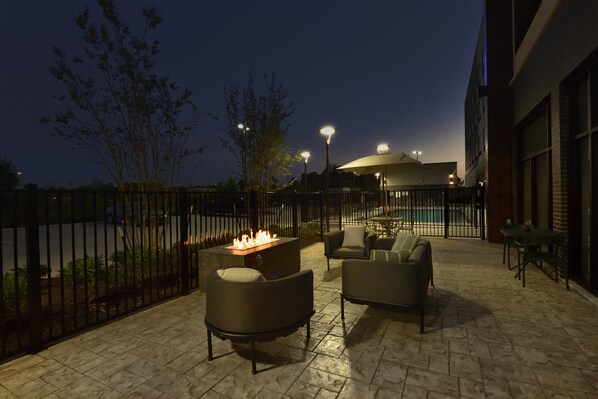 An outdoor patio area with a fire feature, seating, and a pool in the background. - Holiday Inn Express & Suites Spring - Woodlands Area by IHG (Spring)