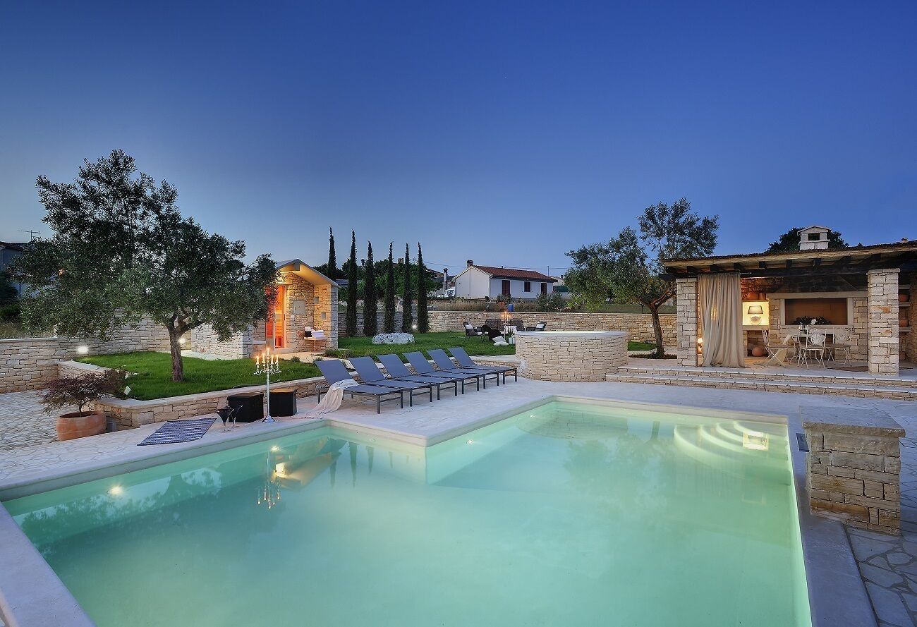 A swimming pool with lounge chairs, a stone wall, and a small building with a tiled roof.