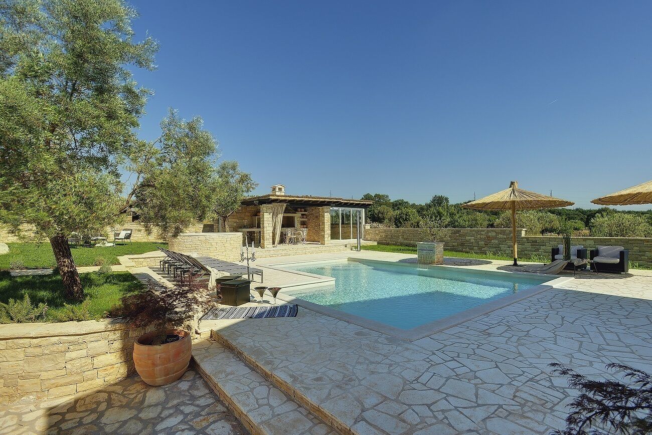 Une piscine avec des carreaux de pierre, un mur en pierre et une pergola agrémentée de parasols.