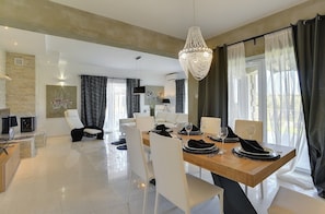 A modern dining area with a wooden table set for four, white chairs, and a chandelier.