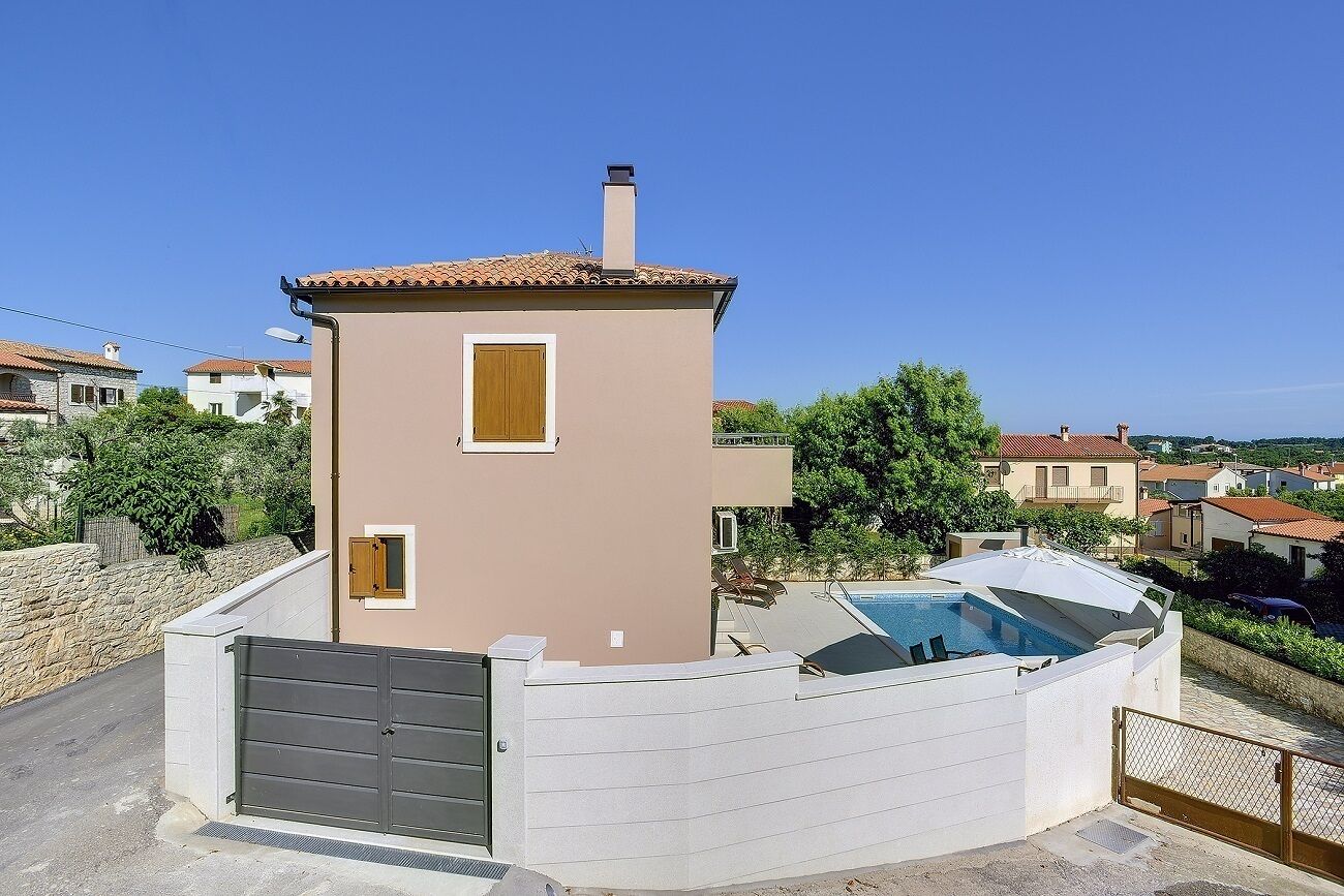 A two-story house with a swimming pool, a gate, and a stone wall.