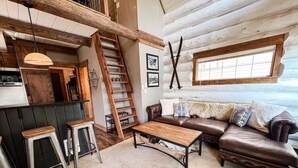 L’intérieur d’un chalet rustique est agrémenté d’un escalier en bois, d’un canapé en cuir, d’une table basse en bois et d’un coin cuisine avec un réfrigérateur.