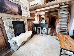 A rustic interior with a stone fireplace, wooden beams, and a loft area with a ladder.