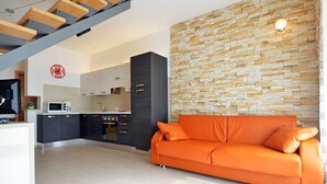 A modern kitchen with dark cabinets, a microwave, and a stove. There is a bright orange sofa and a stone wall in the living area. - Beautiful villa 400 meters to beach with 2 pools (Banjole)