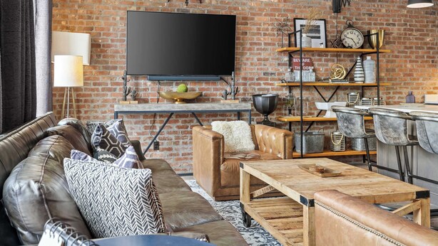 A living room with a brick wall, leather sofa, wooden coffee table, and a television. - Two Luxury WeHo Homes w/ Rooftops + 6BR Near DT (Nashville)