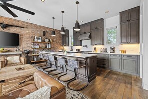 A modern kitchen with a brick wall, bar stools, and a large island. - Two Luxury WeHo Homes w/ Rooftops + 6BR Near DT (Nashville)