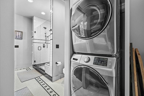 A modern laundry room with stacked washers and dryers, a glass shower enclosure, and a patterned floor.