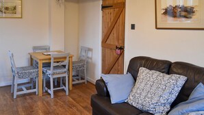 A cozy living room with a wooden dining table, two chairs, a leather sofa with patterned cushions, and a rustic wooden door.