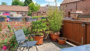 A patio area with a folding chair, potted plants, and a brick wall.