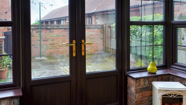 A room with a dark wooden door, a white fireplace, and a view of a brick building outside.