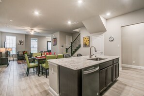 A spacious kitchen with a central island, a dining area with green chairs, and a staircase leading to another level. - Beautiful furnished 3 bedroom Allen Home (Allen)