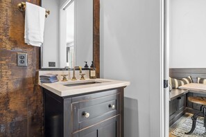 A bathroom with a dark vanity, a white sink, and a mirror. There is a towel hanging on the wall and a bottle of hand soap on the counter. - Luxe WeHo Gem | Rooftop Views • DT • Nightlife (Nashville)