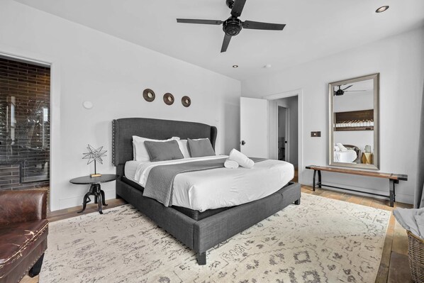 Un dormitorio moderno con una cama grande, un ventilador de techo y un espejo en la pared.