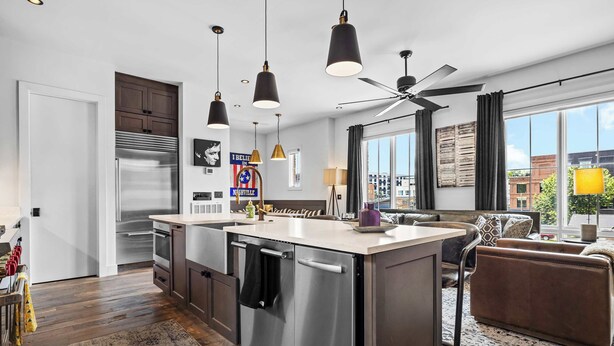 Una cocina moderna con una isla central, electrodomésticos de acero inoxidable, iluminación colgante y un amplio ventanal con vista a la ciudad.