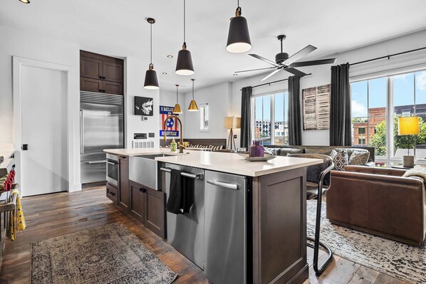 A modern kitchen with a central island, stainless steel appliances, pendant lighting, and a large window with a city view.