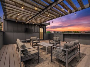 An outdoor seating area with a pergola, cushioned chairs, and a flat-screen TV.
