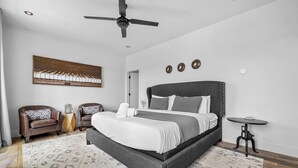 Un dormitorio moderno con una cama grande, dos sillones de cuero, una mesita y un ventilador de techo.