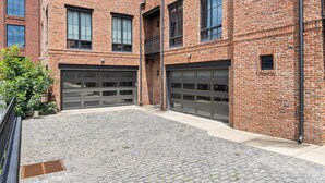 Un edificio de ladrillo con dos puertas de garaje, un patio pavimentado y una cerca de metal.