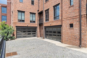 A brick building with two garage doors, a paved courtyard, and a metal fence.