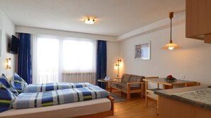 Een compacte hotelkamer met een bed, een eettafeltje, een stoel en een kitchenette.