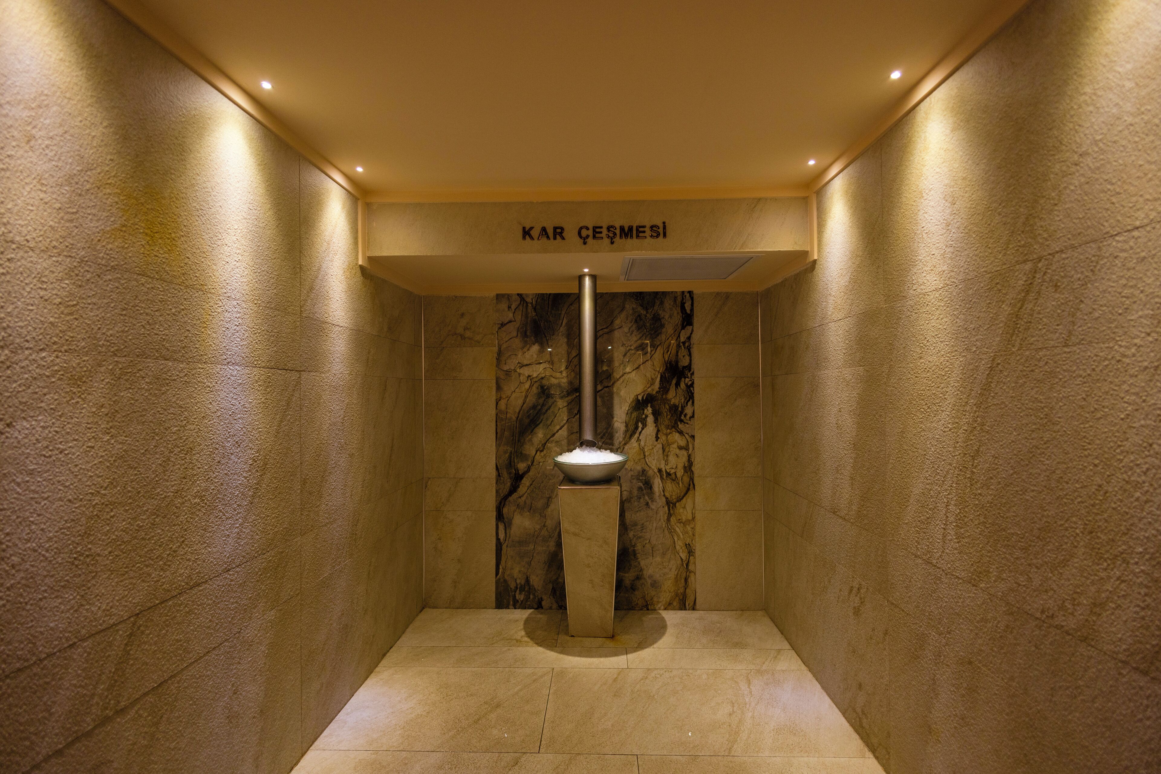 Un baño con pared de mármol, un lavamanos pedestal y un letrero sobre el lavamanos que dice "KAR ÇESMESİ".