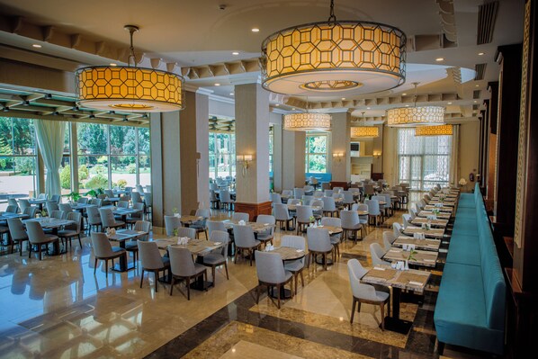 A spacious hotel dining area with multiple tables and chairs, large windows, and decorative lighting fixtures. - Ramada Plaza by Wyndham Mardin (Mardin)