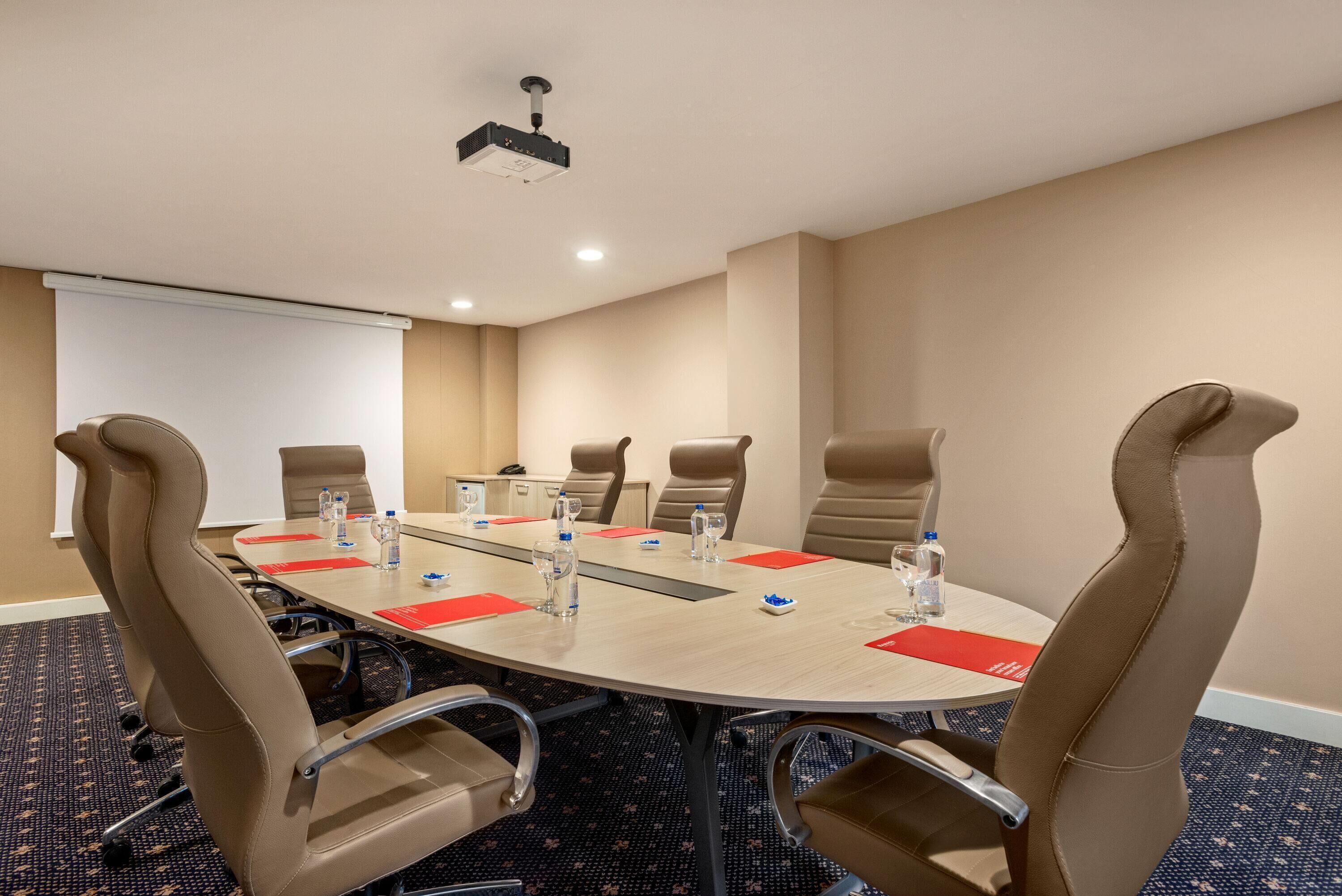 A conference room with a round table, six chairs, a projector, and a whiteboard.