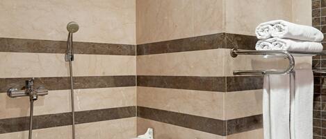 A bathroom with a shower, a white grab bar, and a towel rack with folded towels.