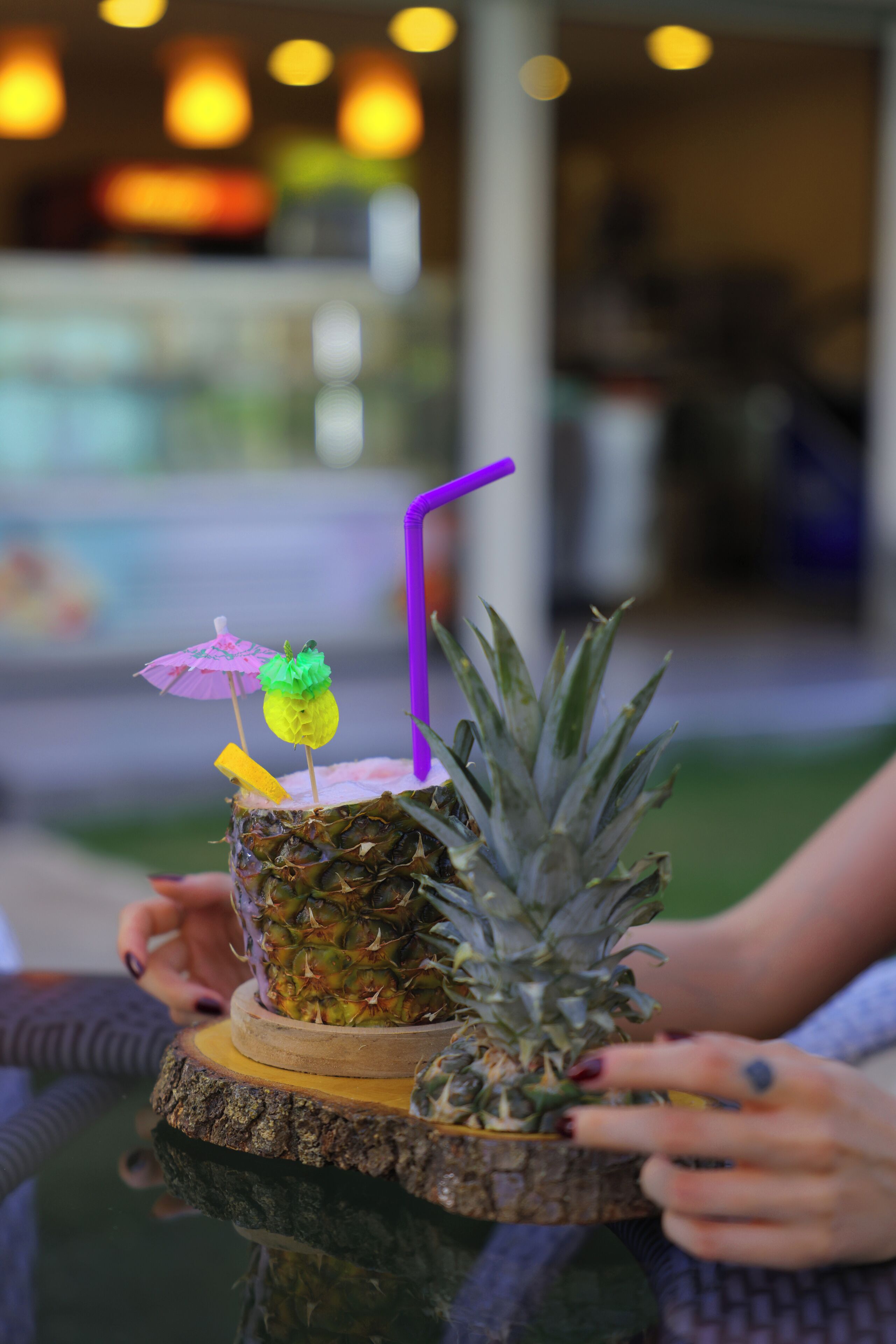 A pineapple drink on a wooden coaster with a purple straw and a small umbrella.