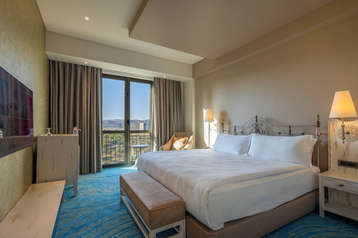 Habitación de hotel con una cama grande, un banco, un escritorio y vistas al exterior.