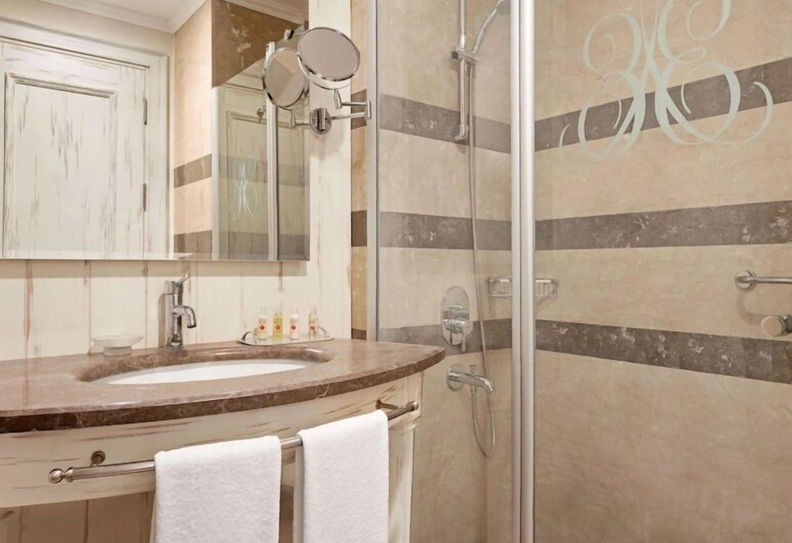 A bathroom with a marble sink, a mirror, a towel rack, and a shower with a glass door.