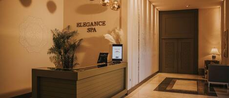 Una reception con una insegna a parete che recita 'ELEGANCE SPA', una pianta in vaso e uno schermo digitale che mostra un logo.
