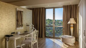 A hotel room with a desk, chair, lamp, and a view of a balcony with curtains.