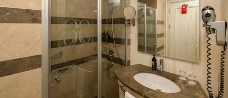 Un baño moderno con ducha envuelta en cristal, lavamanos con encimera de mármol y un secador de pelo montado en la pared.