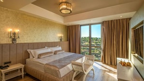 A hotel room with a large bed, a bedside table, a chair, a desk, and a view of the outdoors.