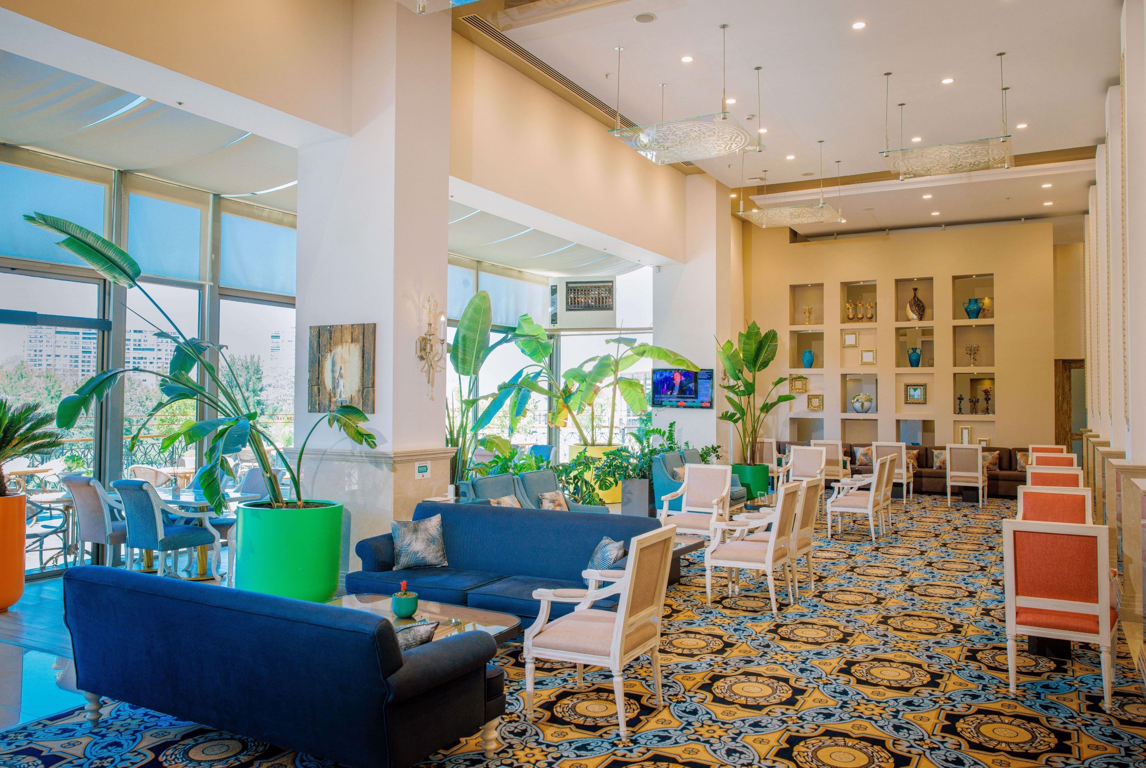 A hotel lobby with seating areas, large windows, and a patterned carpet.