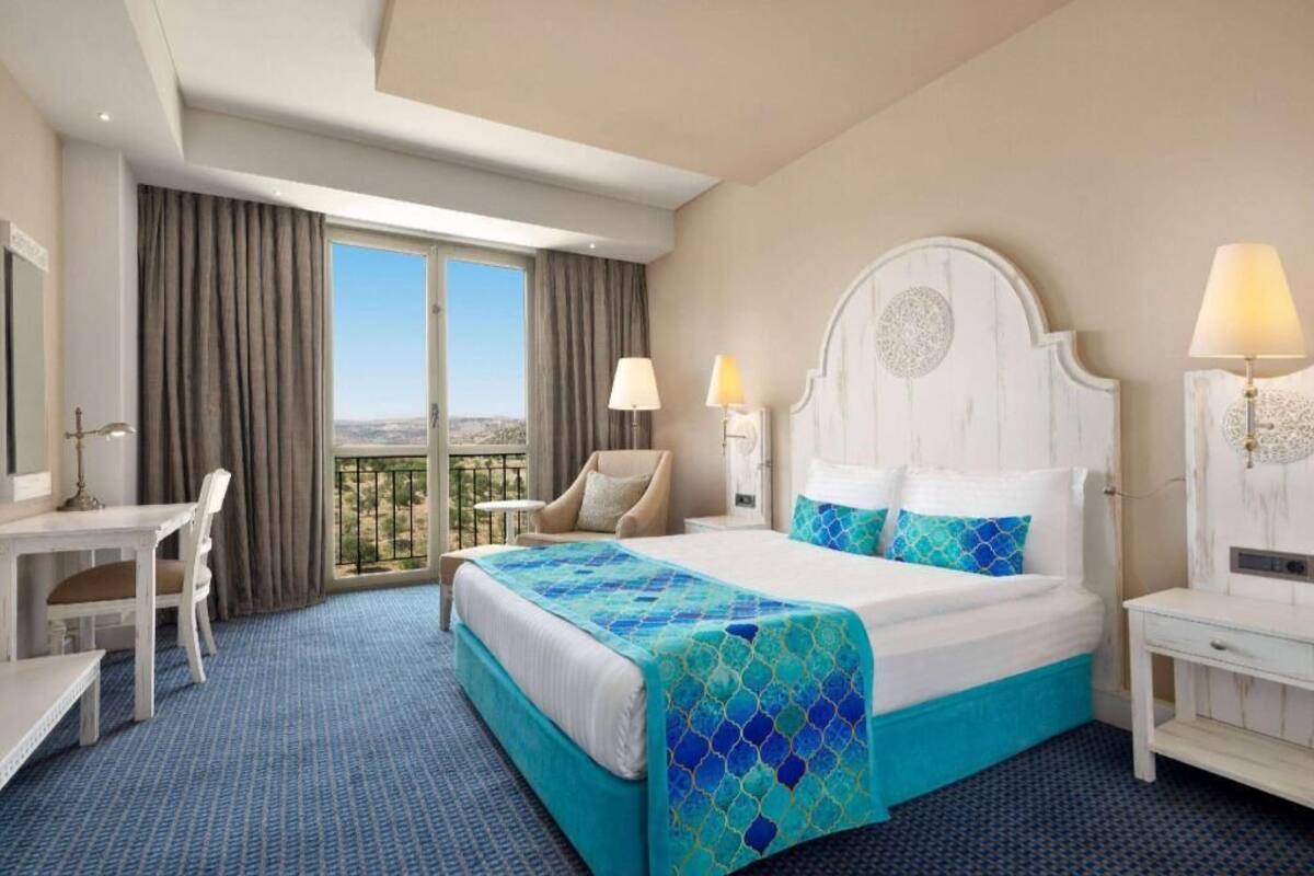 Habitación de hotel con una cama grande, un escritorio, una silla y un balcón con vistas.