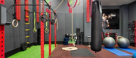 Uma academia com equipamentos em vermelho e preto, um saco de pancada e bolas de exercício.