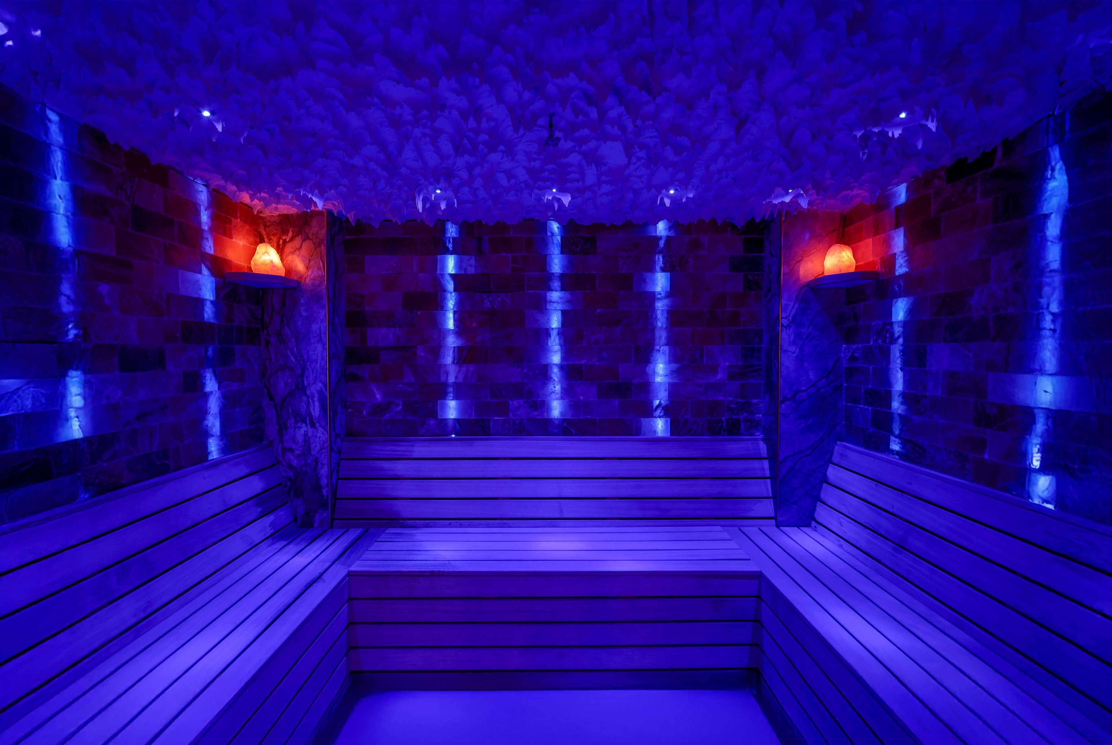 A sauna with wooden benches and stone walls, illuminated by blue lighting.
