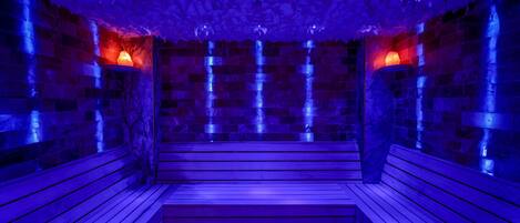 A sauna with wooden benches and stone walls, illuminated by blue lighting.