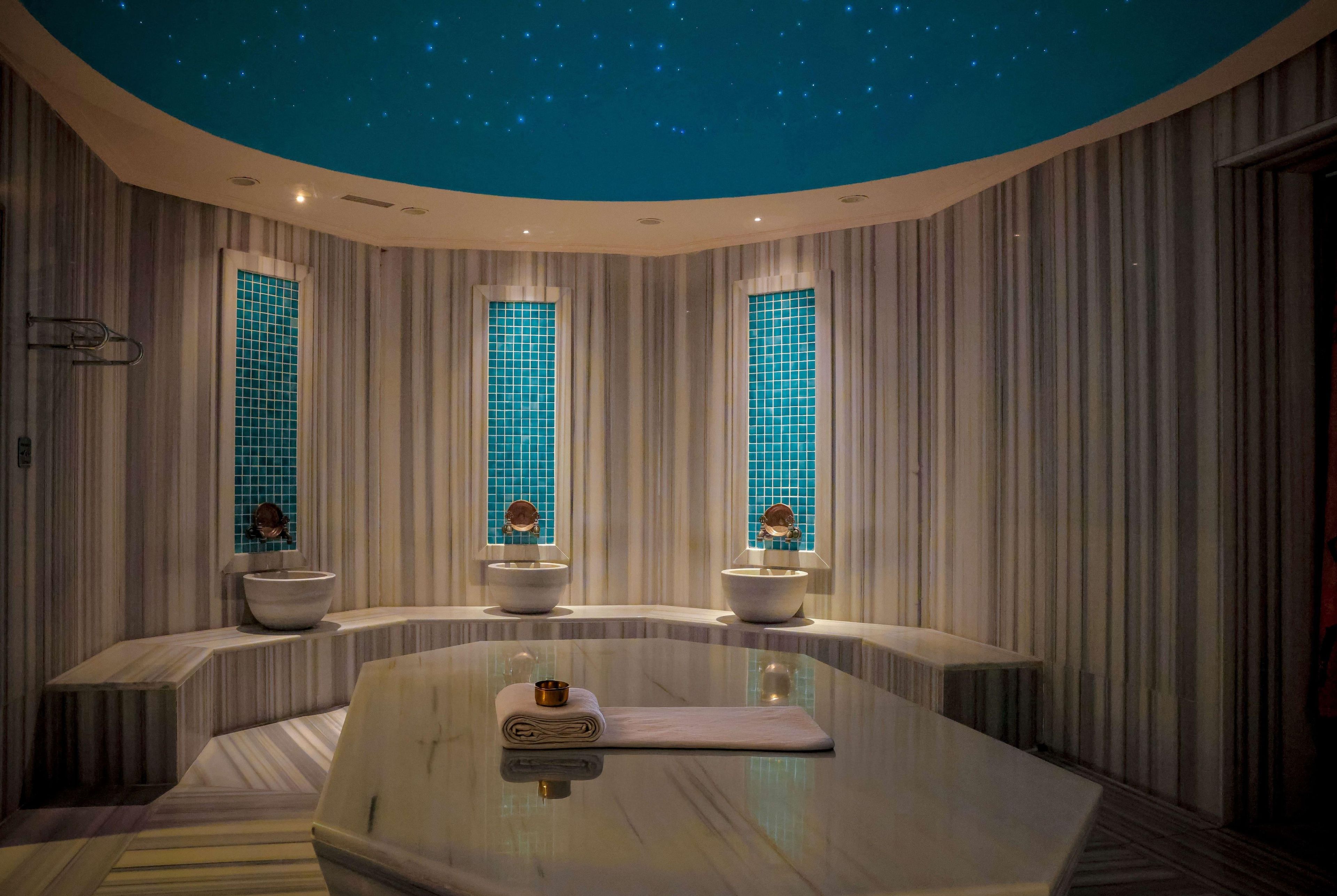 A modern bathroom with a curved vanity, a large mirror, and three windows with blue-tiled frames.