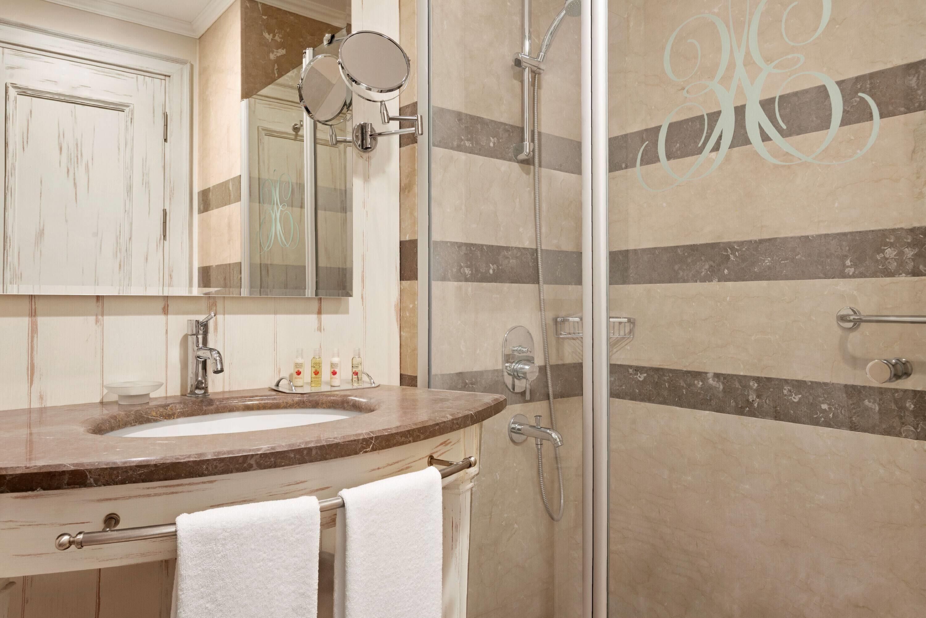 Un baño con lavabo de mármol, un espejo grande, cabina de ducha de cristal y un perchero para toallas.
