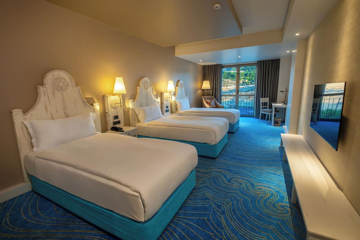 Habitación de hotel con tres camas, un escritorio, una silla y un televisor.