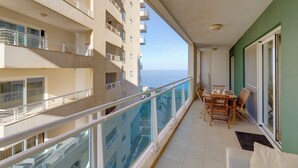 Un balcón con una mesa y sillas, con vistas a un edificio de varios balcones y al mar.