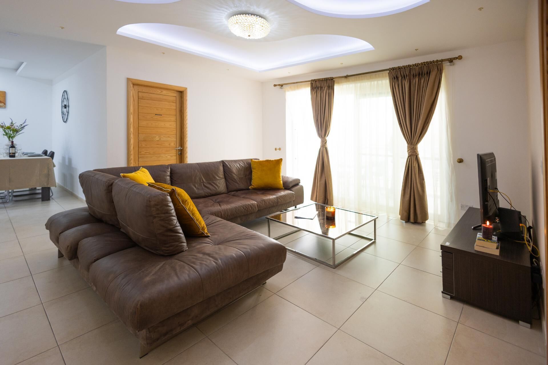 A living room with a brown leather sofa, a glass coffee table, and a TV stand.