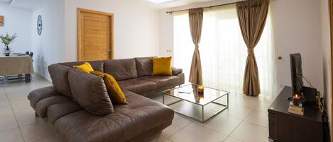 A living room with a brown leather sofa, a glass coffee table, and a TV stand.