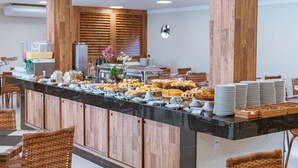 A buffet setup with various food items, wooden cabinets, and wicker chairs. - Orquídeas Praia Hotel (Porto Seguro)