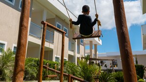 A child on a swing set in a courtyard with a building in the background. - Orquídeas Praia Hotel (Porto Seguro)