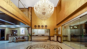 Um hall amplo com um lustre imponente, um balcão de recepção e um padrão circular decorativo no chão.