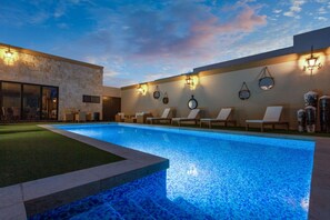 A swimming pool with lounge chairs and wall-mounted lights.